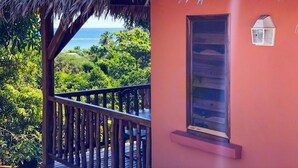 Ein Zimmer mit einem Strohdach, einem Fenster mit einer weißen Laterne und Blick auf das Meer und die grüne Landschaft.