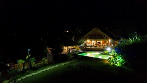 Ein gut beleuchtetes Lodgehaus mit Pool, umgeben von üppigem Grün.