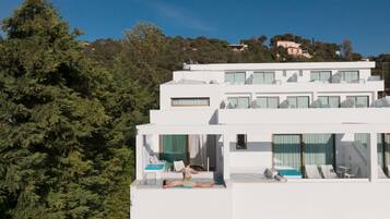 A modern building with multiple balconies and large windows, surrounded by dense greenery.