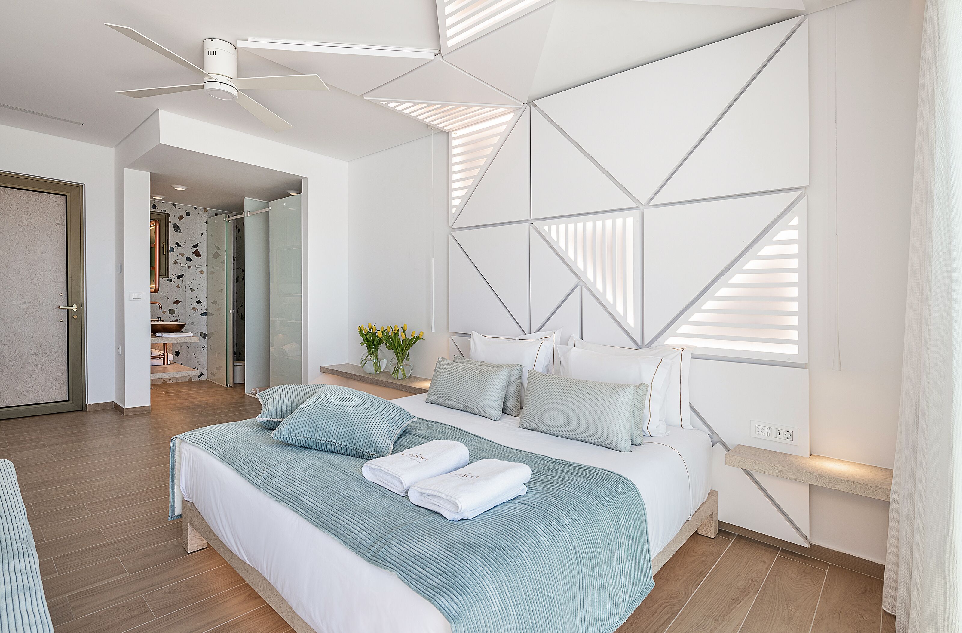 A modern bedroom with a large bed, a ceiling fan, and a geometric wall design.