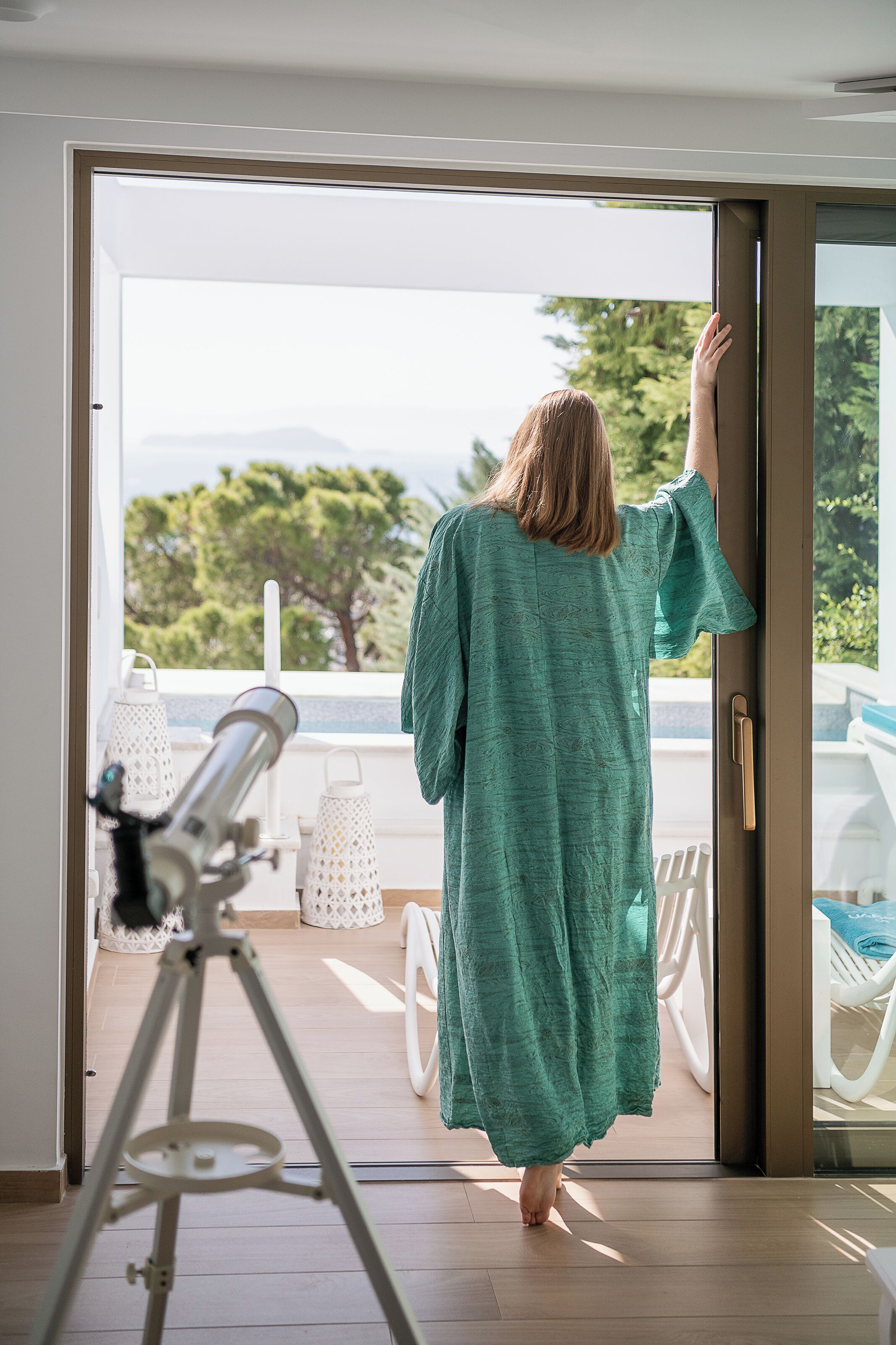 A person in a green dress standing at an open door, looking outside.