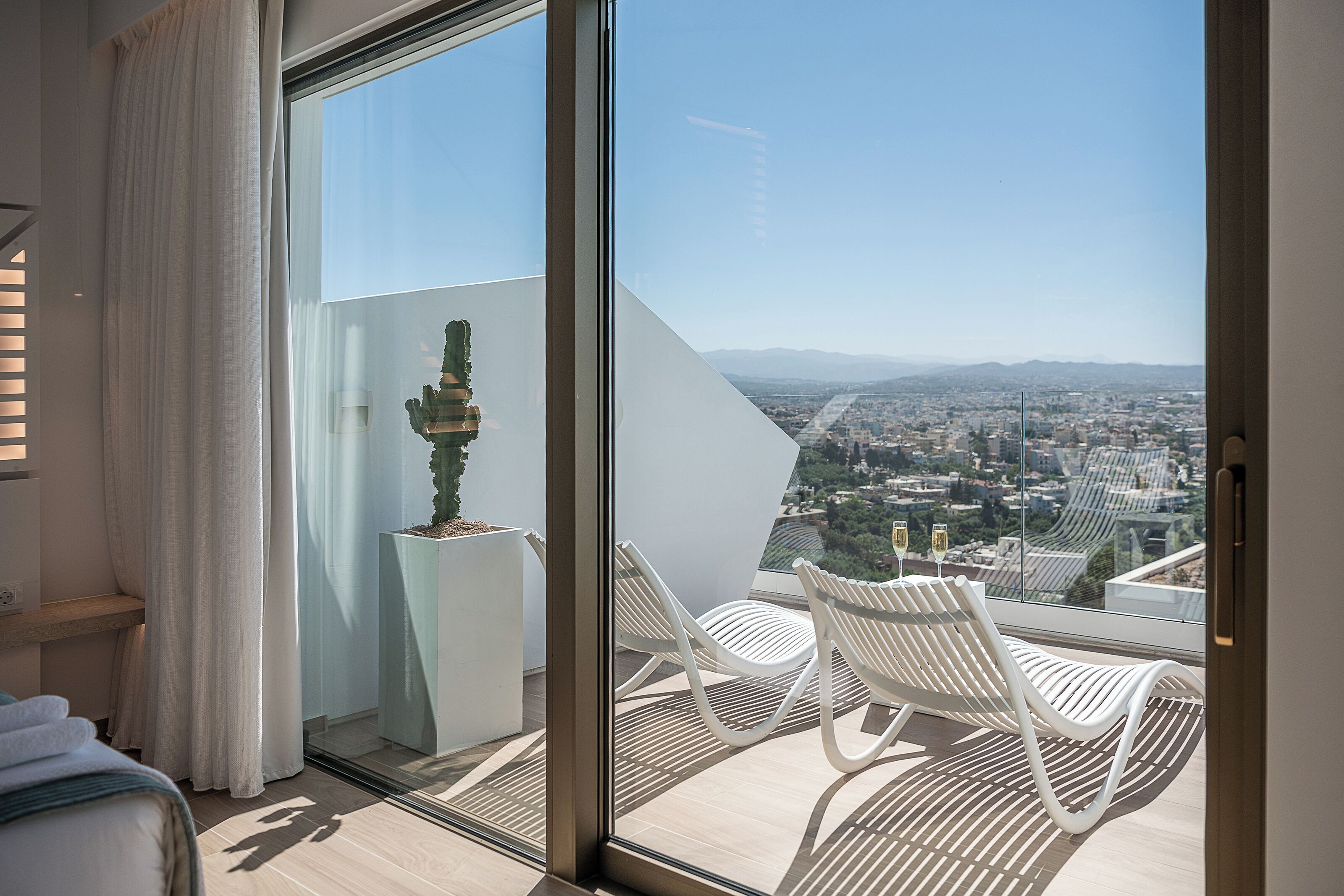 Ein Balkon mit Blick auf die Stadt, weißen Stühlen, einem Blumentopf und einem Bett mit weißem Kopfteil.