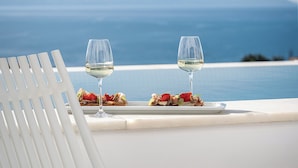 Una silla y una mesa con dos copas de vino blanco y un plato de comida en un balcón con vista al mar.