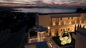 Un edificio moderno con terraza en la azotea, mobiliario exterior y una original escultura de luz.