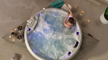 A hot tub with a person relaxing, surrounded by decorative candles and a potted plant.