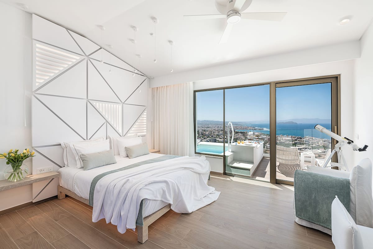 Un dormitorio moderno con una cama grande, vistas de la ciudad y un balcón con un telescopio.