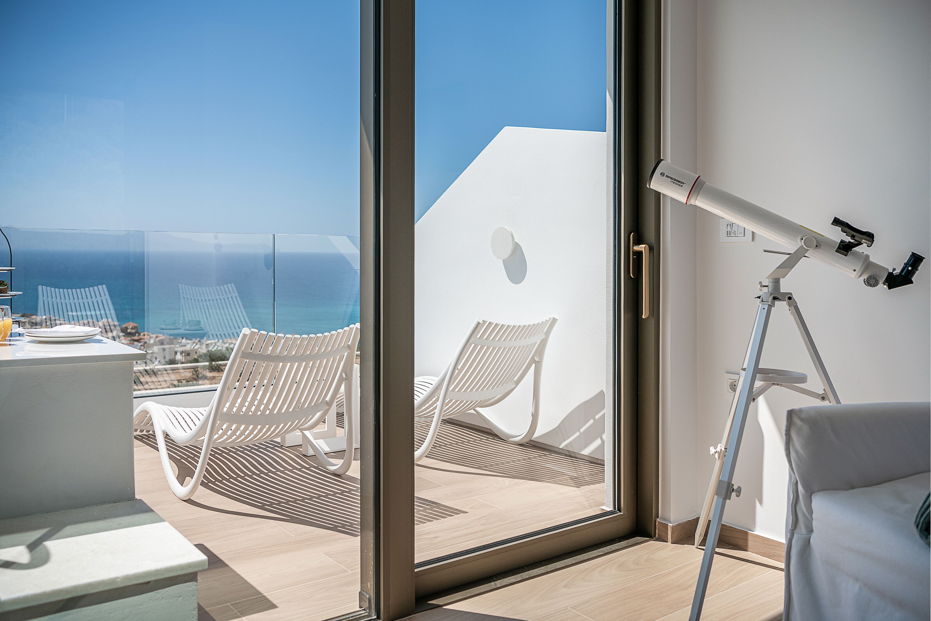 Une chambre moderne dotée d’une grande porte vitrée donnant sur un balcon avec des chaises et une table blanches.