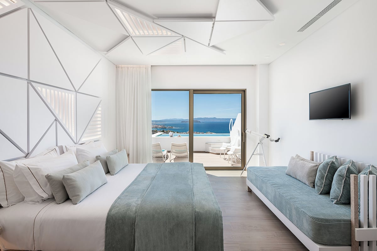 Habitación de hotel moderna con una cama grande, un sofá y un balcón con vistas al mar.