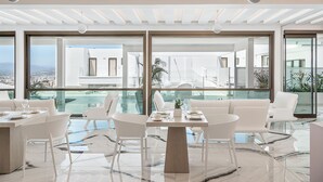 Un comedor moderno con piso de mármol, mobiliario blanco y grandes ventanales con vista a la ciudad.