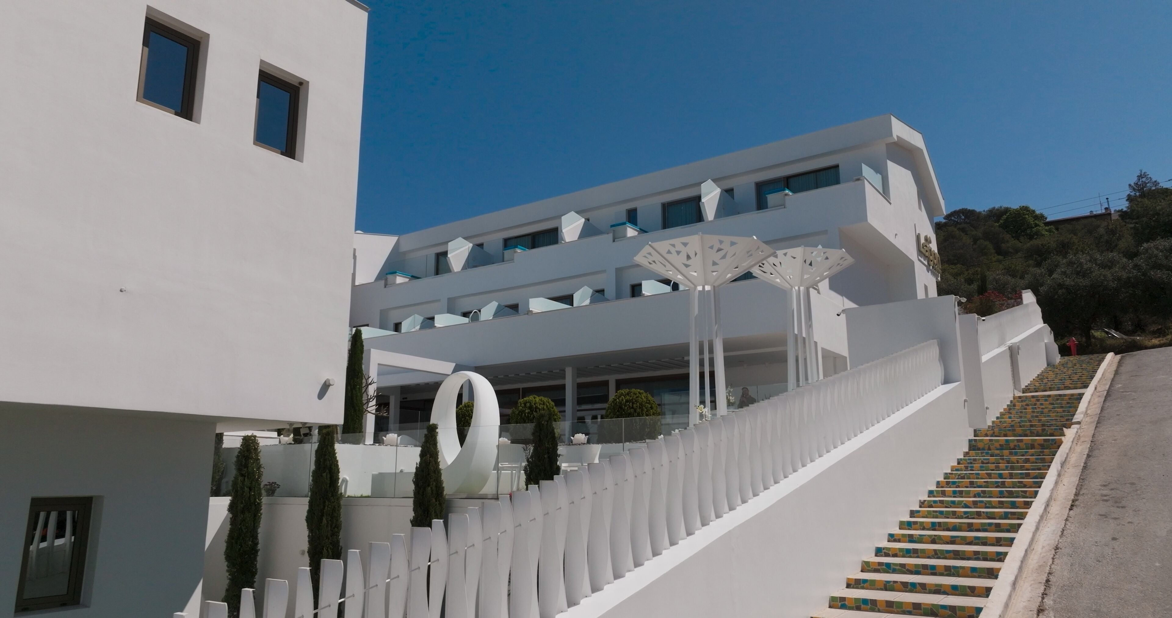 Un edificio moderno con fachada blanca, una escalera que sube a un segundo piso y una gran estructura circular cerca de la entrada.