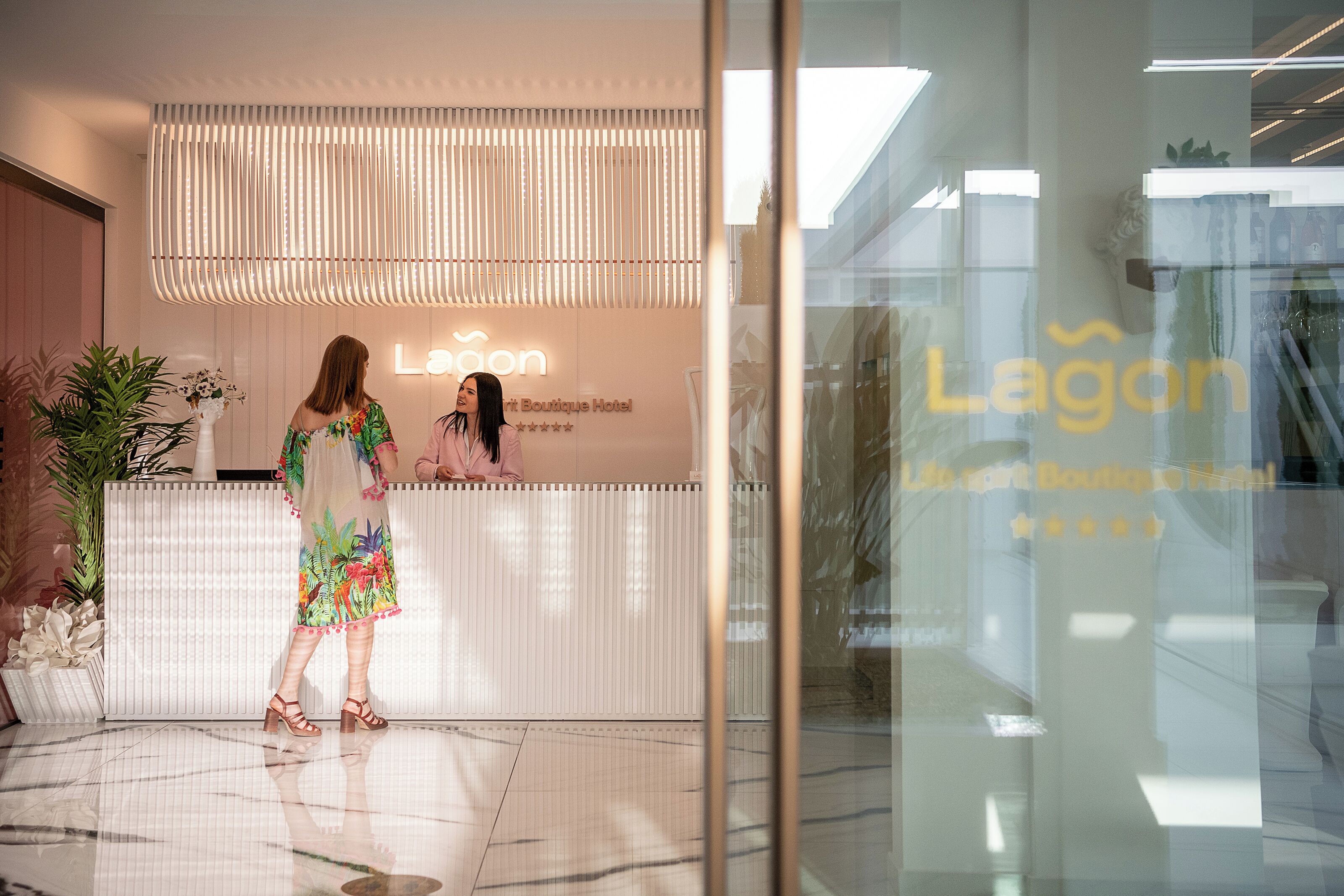 Ein Hotel-Empfangsbereich mit modernem Design, der einen Empfangstresen, eine Glaswand und ein Schild mit der Aufschrift "Lagoon Boutique Hotel" zeigt.