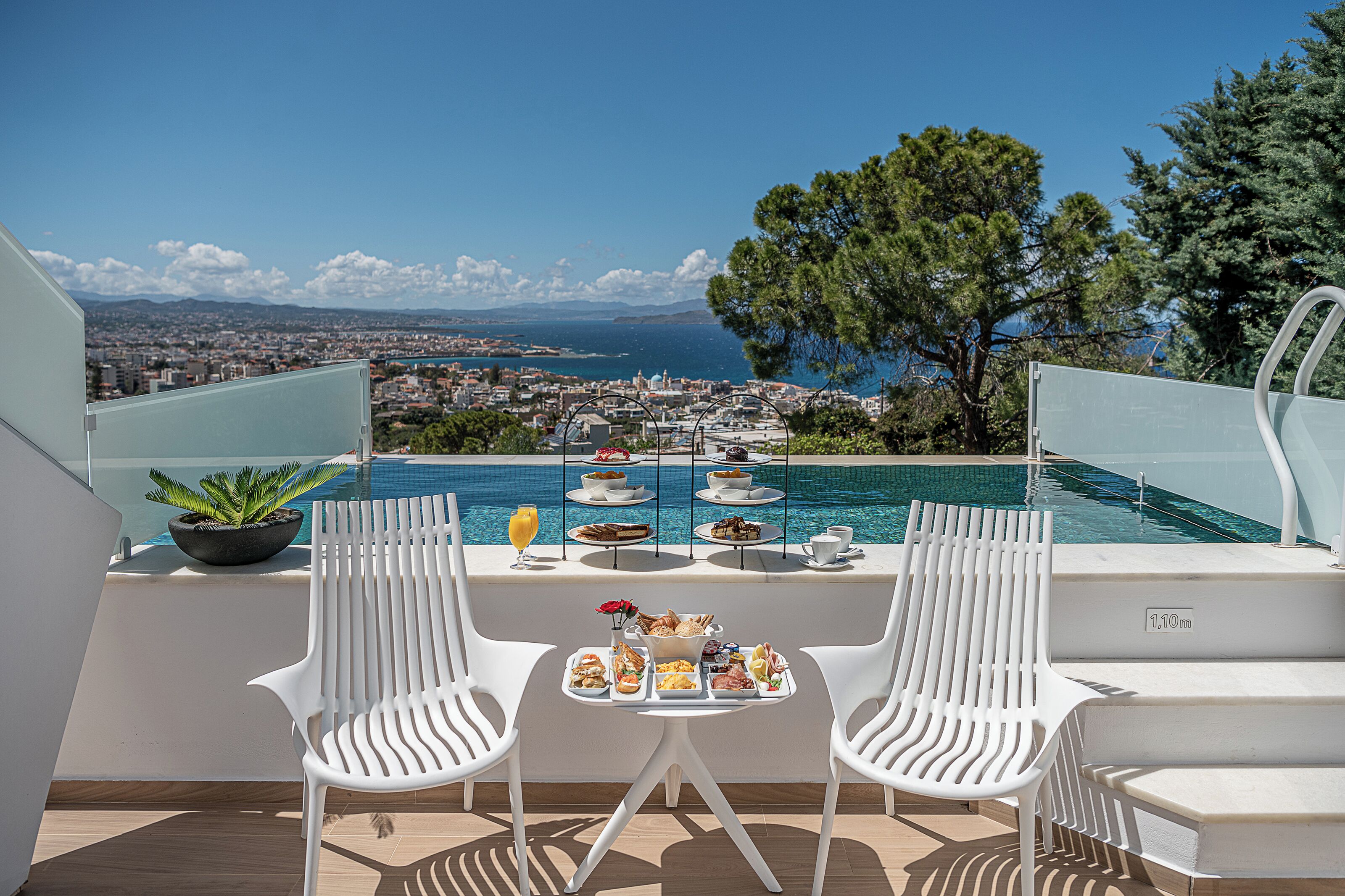 A rooftop terrace with a dining table set for two, overlooking a city and the sea.