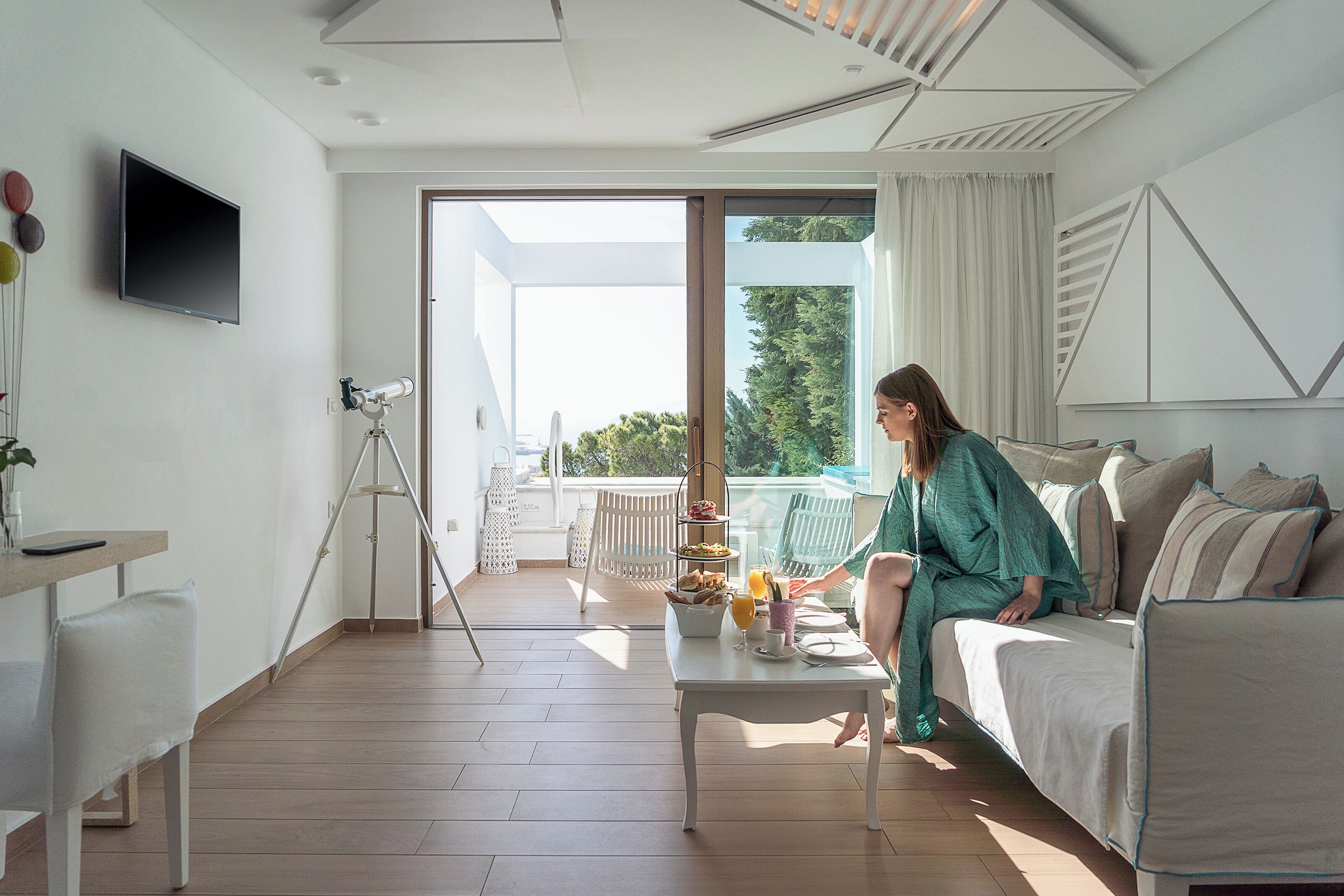 Una sala de estar moderna con un sofá, una mesita de centro con alimentos para el desayuno, un telescopio y un balcón con mobiliario exterior.