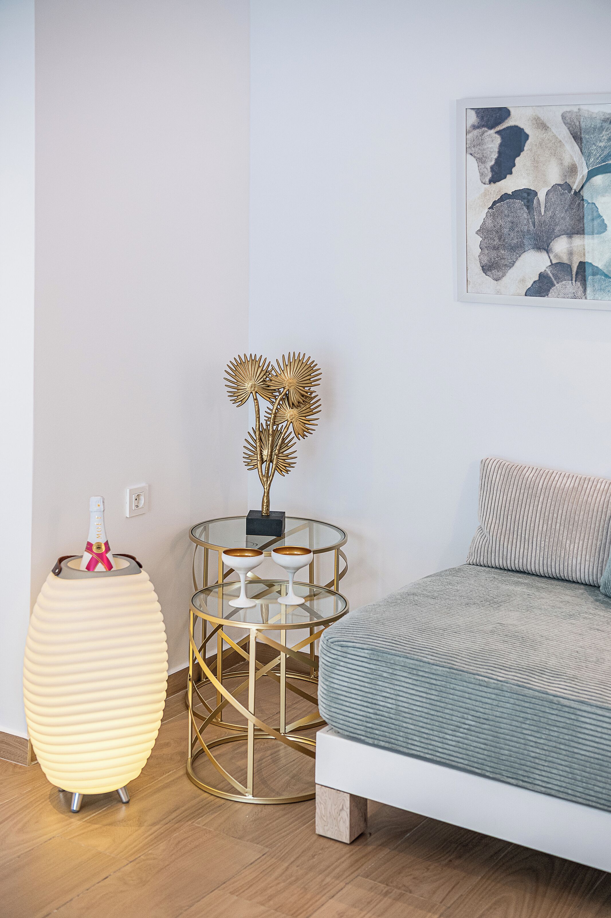 A modern bedroom with a bed, a round glass table with golden accents, a decorative vase, and a champagne bottle.