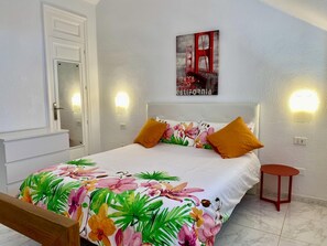 A bedroom with a bed, a nightstand, a door, and a wall-mounted light.