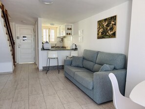 Een moderne woonkamer met een grijze bank, een witte stoel en een keuken met witte kasten en een koffieapparaat.