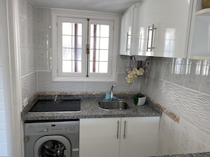 Een kleine keuken met een ingebouwde wasmachine en droger, een spoelbak en een raam met gordijnen.