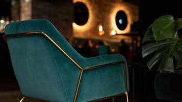 A teal upholstered chair with a gold frame, positioned in a dimly lit room with a modern, circular light fixture in the background.