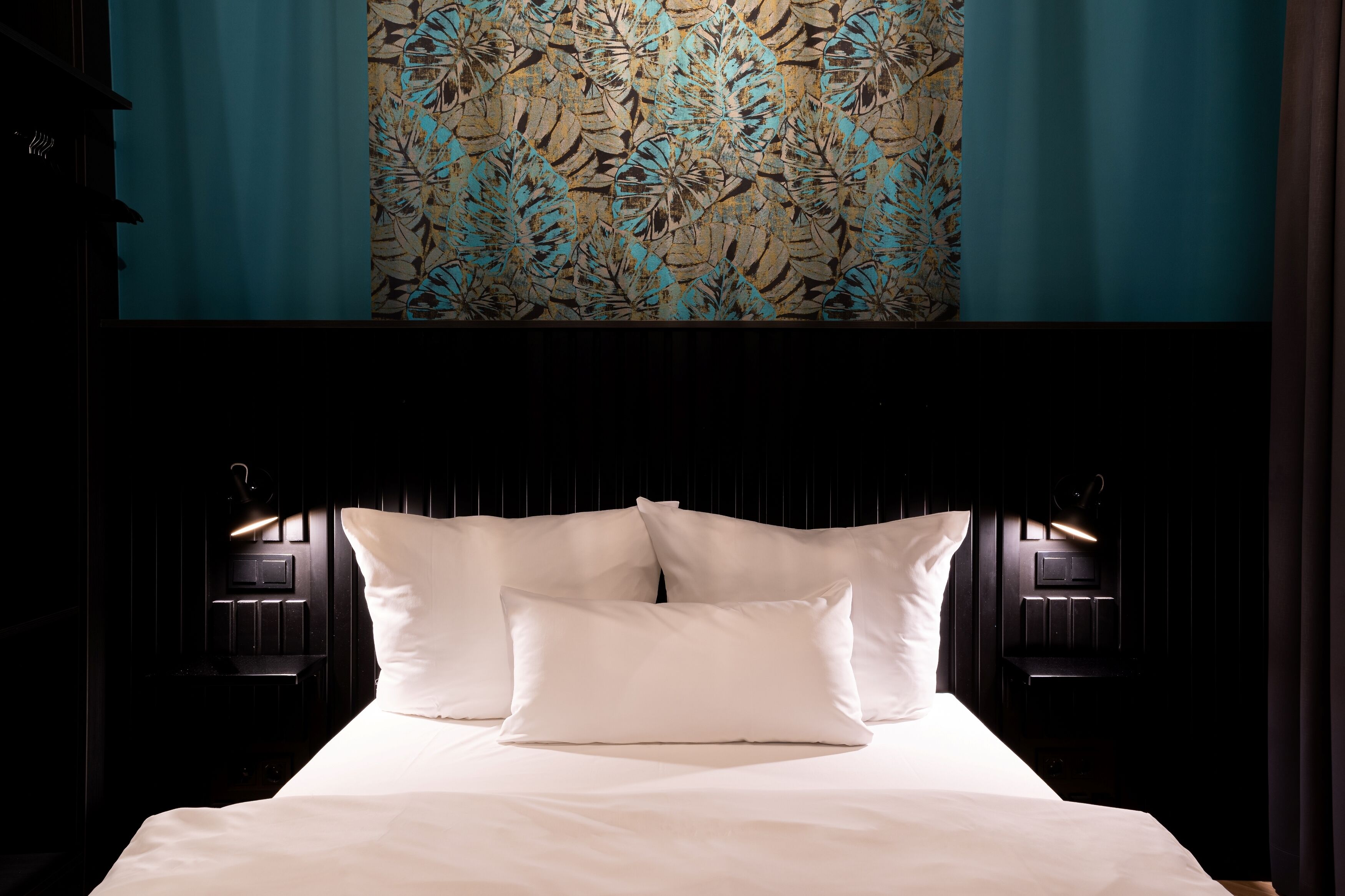 A neatly made bed with white linens and two pillows, flanked by two bedside tables with wall-mounted lamps.
