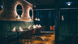 A restaurant with brick walls, green upholstered booths, and wooden flooring.