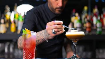 Ein Barkeeper bereitet Getränke an der Bar zu, im Hintergrund sind verschiedene Flaschen zu sehen.