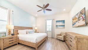 A bedroom with a wooden bed, nightstands, a dresser, a ceiling fan, and a large window.