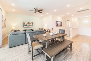 A spacious living area with a dining table, sofas, and a ceiling fan.