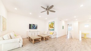 A spacious living room with a white sofa, a coffee table, and a TV mounted on the wall. - It's All Fin & Games Cottage with Private Pool near Disney & Margaritaville. (Kissimmee)