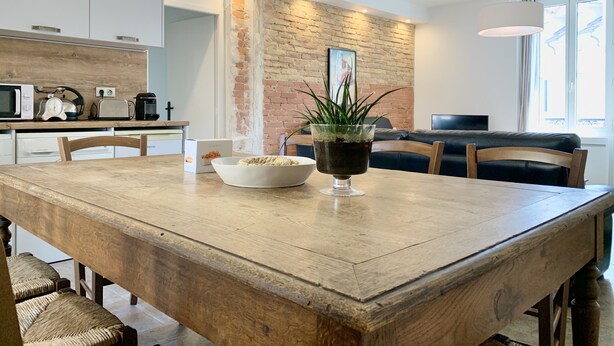 A modern kitchen with white cabinets, a wooden dining table, and a brick accent wall.