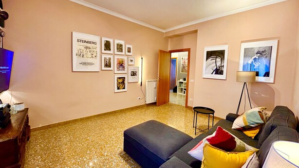 Un salon avec un canapé, une table basse et un téléviseur. Des tableaux encadrés ornent le mur, et une porte donne accès à une autre pièce.