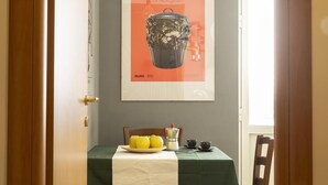 Un coin repas avec une table dressée pour deux personnes, une affiche accrochée au mur et une fenêtre laissant entrer la lumière naturelle.