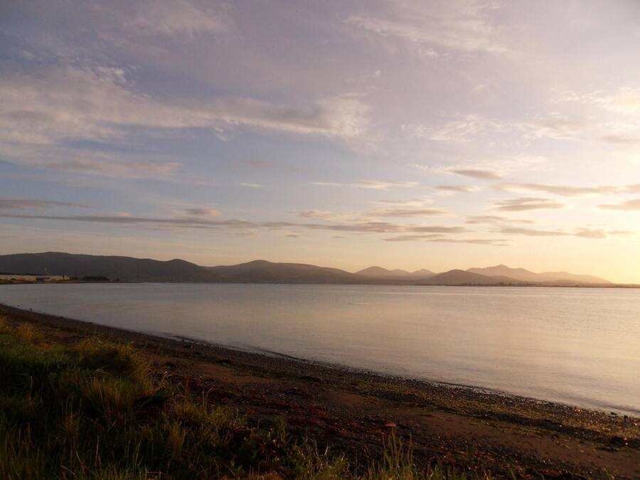 Um lago tranquilo com montanhas ao fundo e uma margem gramada.