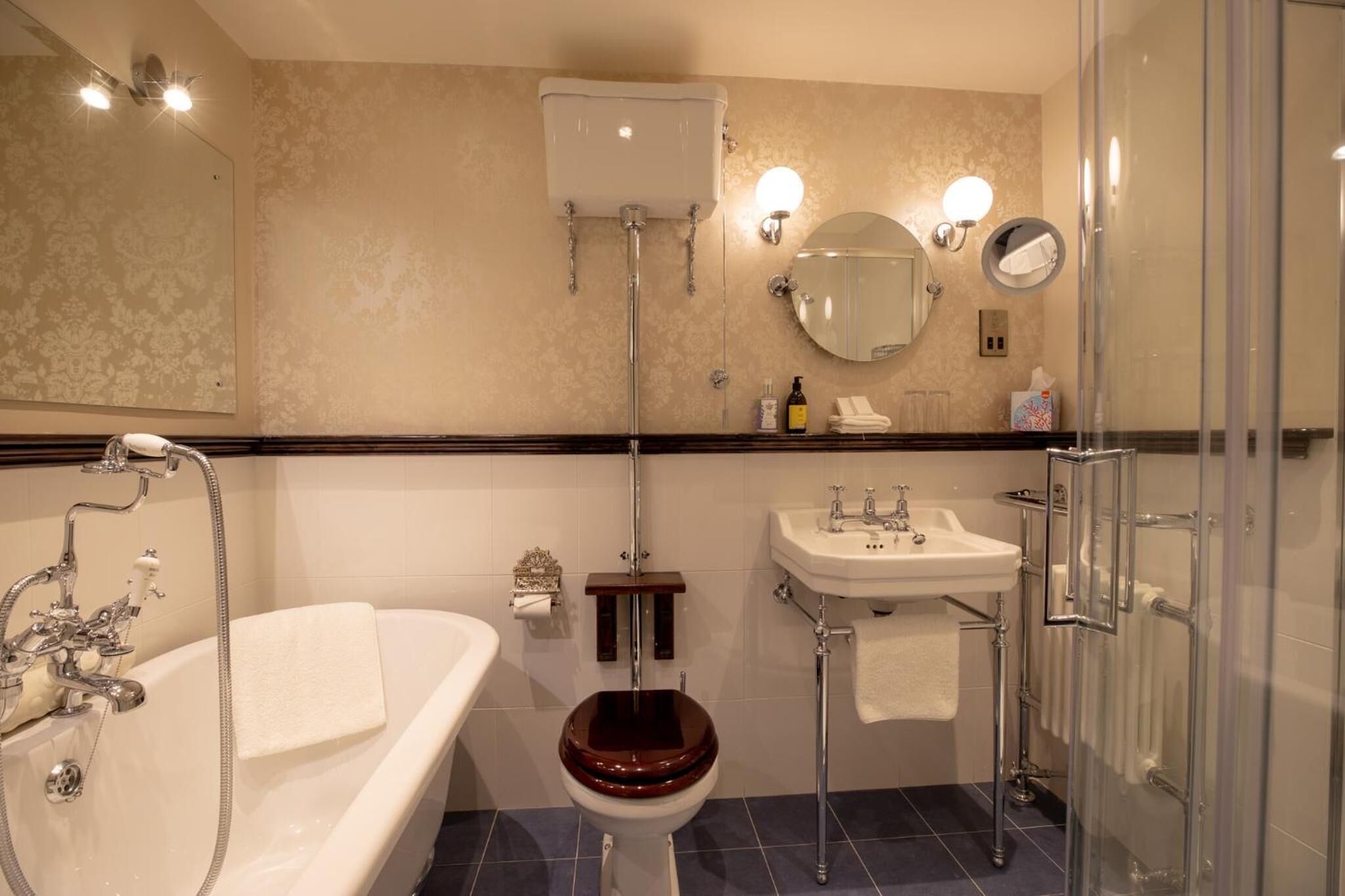 Et badeværelse med badekar, toilet, vask og glasvæg omkring brusebadet.