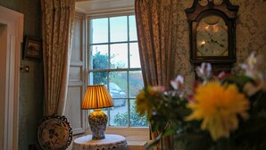 A room with a window, curtains, a clock, a lamp, and a vase with flowers. - Ghan House Carlingford (Carlingford)
