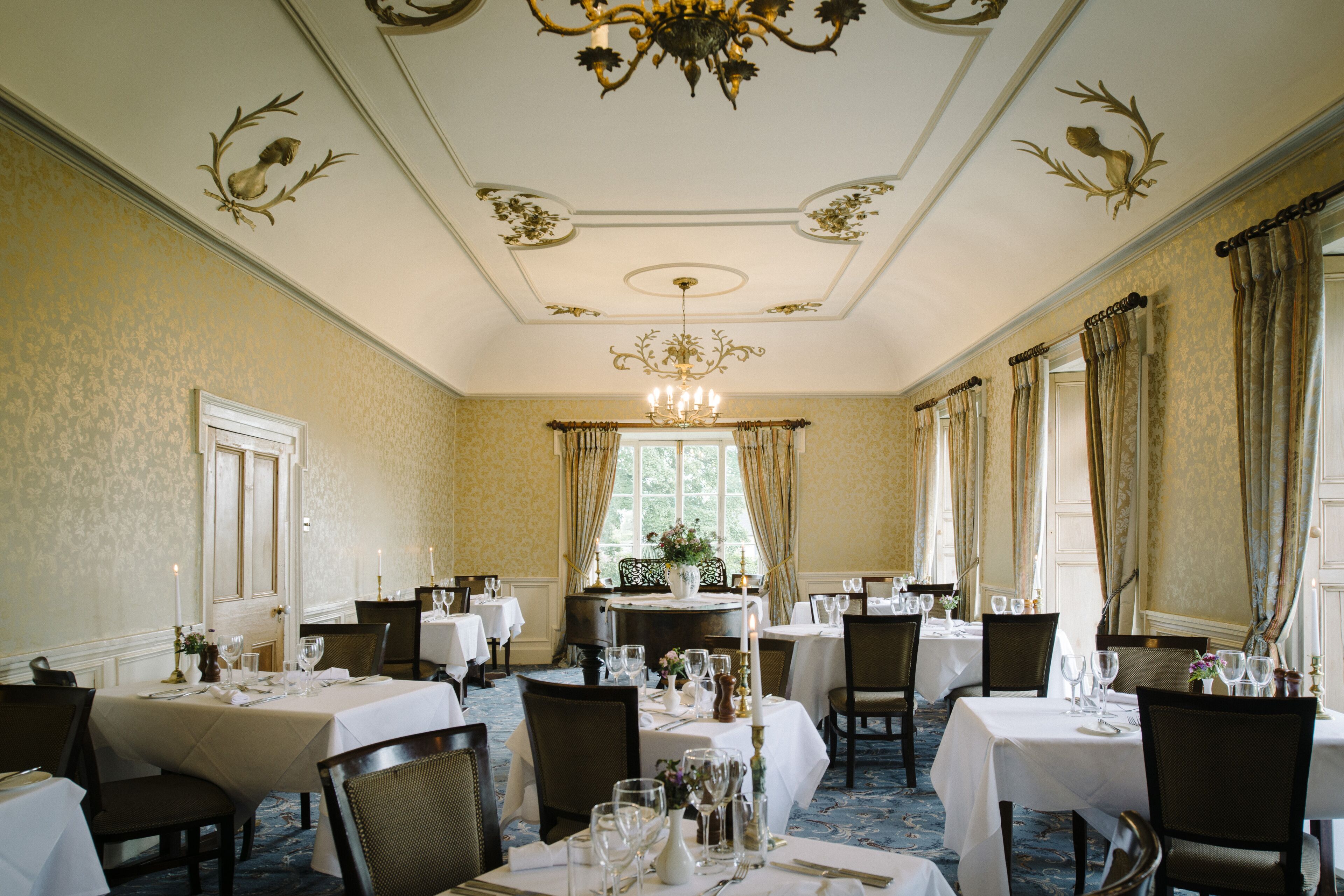Un comedor formal con varias mesas dispuestas para el servicio, candelabros elegantes y decoración clásica.
