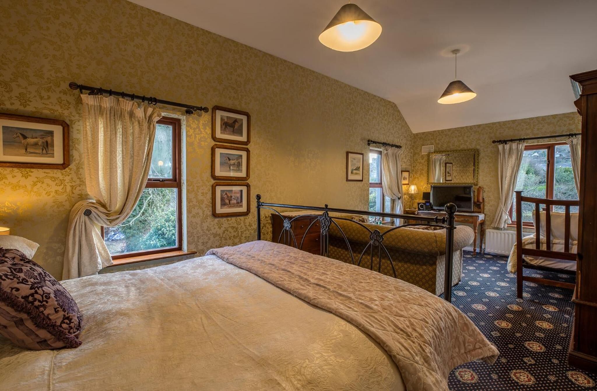 A bedroom with a large bed, a desk with a chair, a television, and framed pictures on the wall.