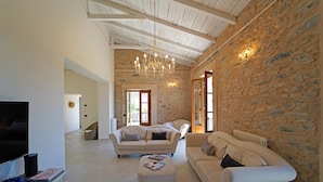 A spacious living room with a large TV, comfortable sofas, a coffee table, and a stone wall. - ** LAST MINUTE ** VILLA VITTORIA (sleeps 8), by Villas & Retreats: Pool, A/C, Wi-Fi, BBQ (Licciana Nardi (MS))