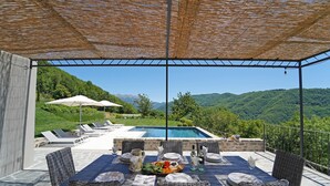 An outdoor dining area with wicker furniture, a pool, and a view of green hills. - ** LAST MINUTE ** VILLA VITTORIA (sleeps 8), by Villas & Retreats: Pool, A/C, Wi-Fi, BBQ (Licciana Nardi (MS))