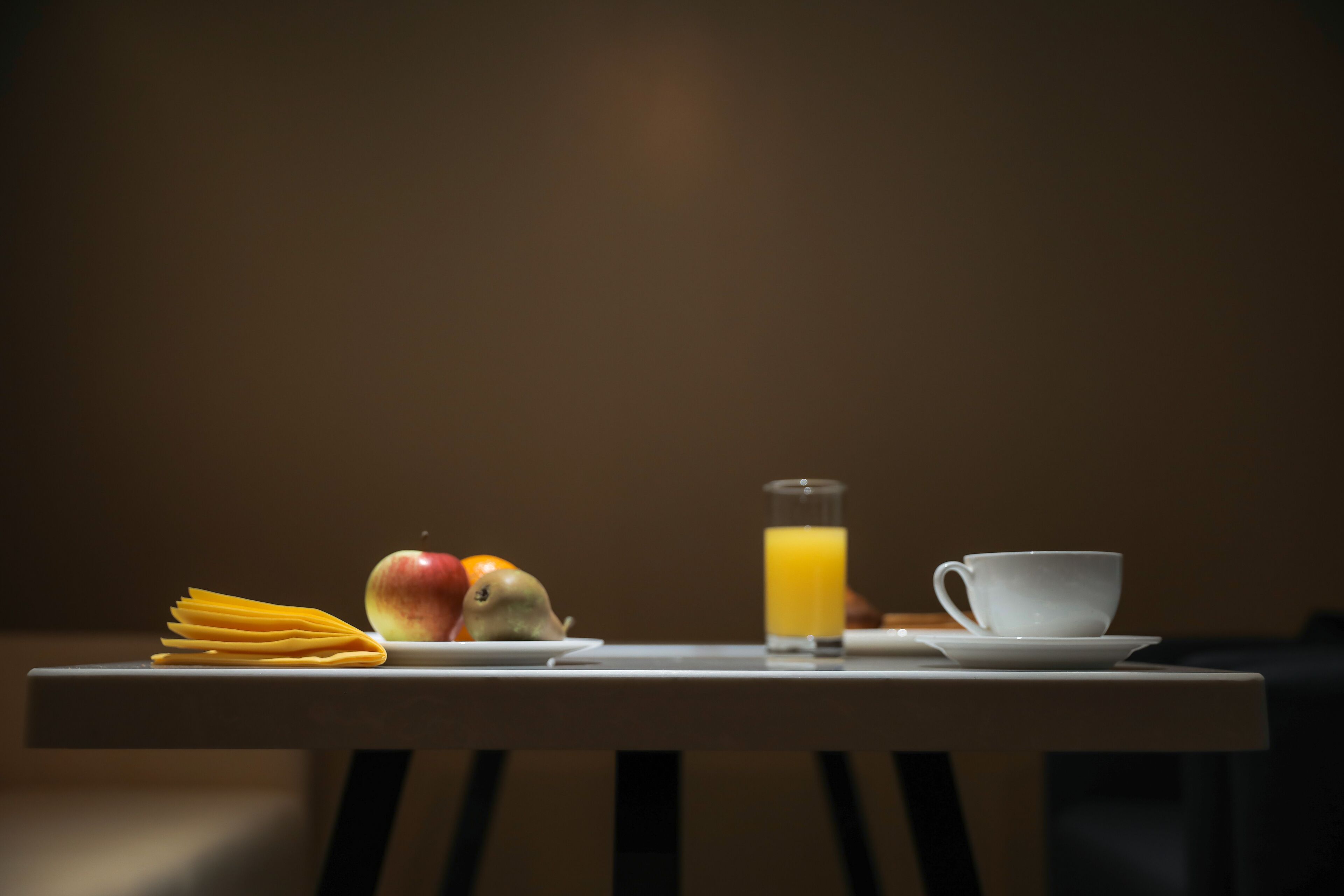 A table with a plate of spaghetti, an apple, a glass of orange juice, and a white cup.