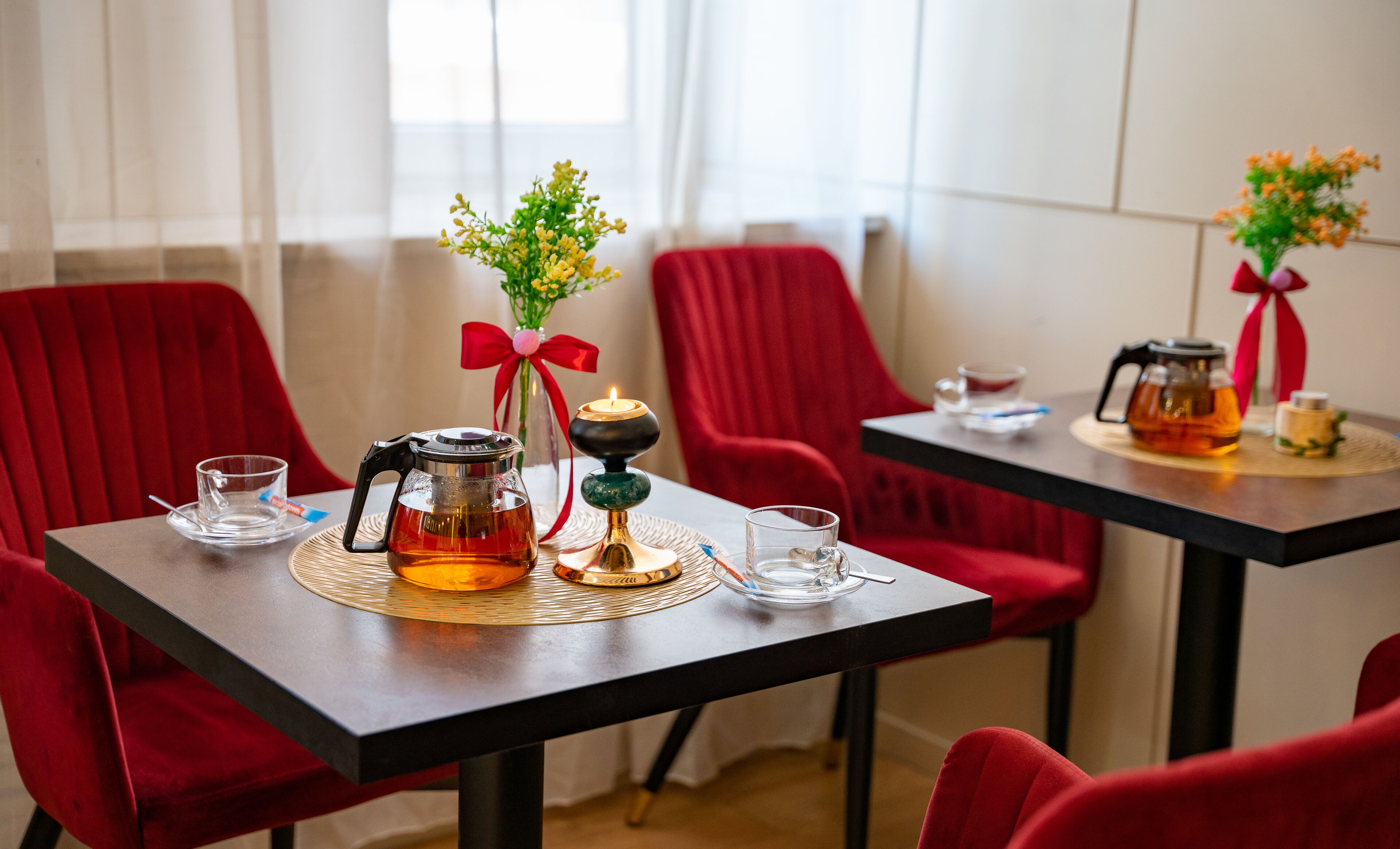 Una mesa de comedor con una tetera, vasos y una vela. Hay sillas rojas alrededor de la mesa.