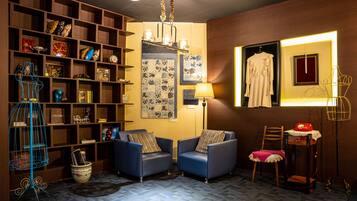 Una habitación acogedora con una estantería de madera, dos sillones azules, una lámpara de pie y una mesita con un teléfono rojo.