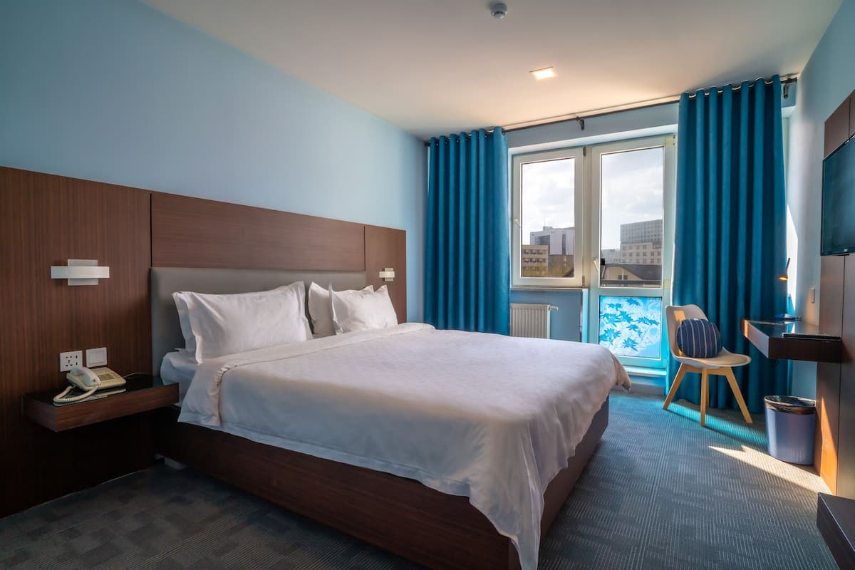 A hotel room with a large bed, a desk with a chair, a TV, and a window with curtains.