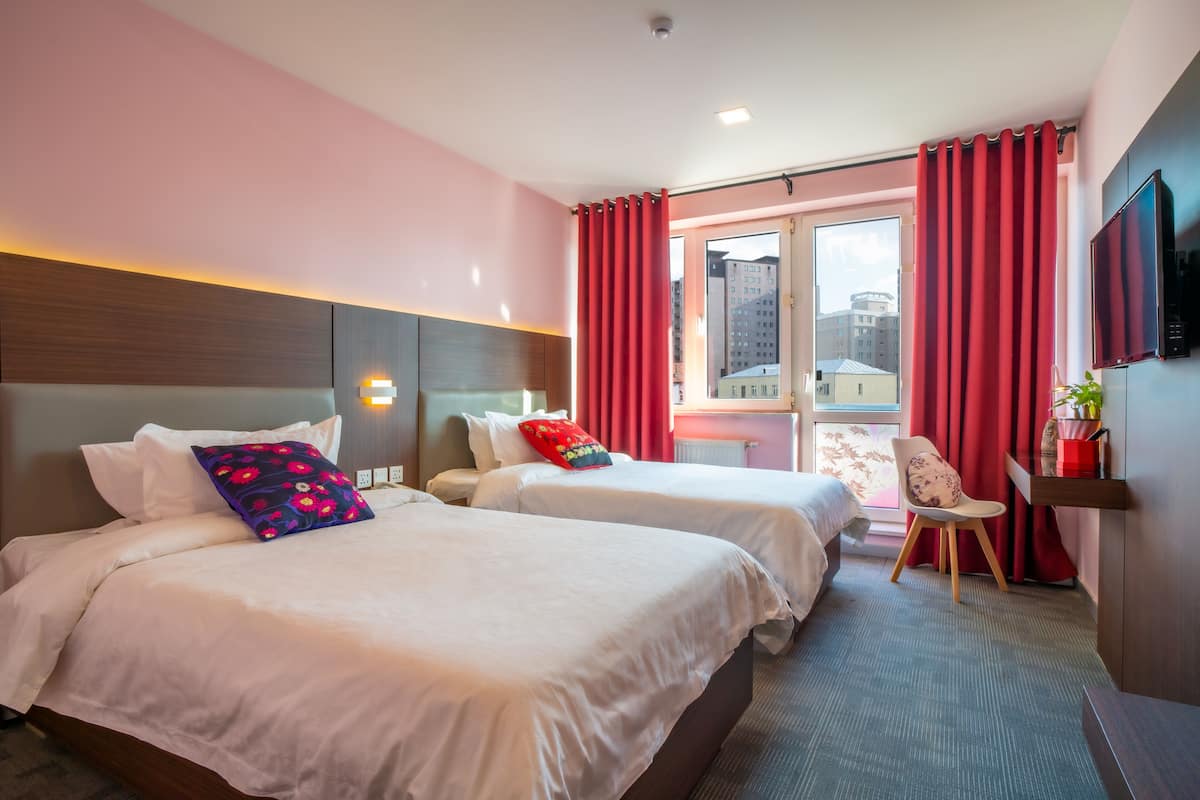 A hotel room with two beds, a desk, a chair, and a TV.