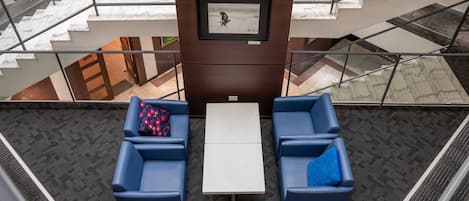 A modern lobby with a marble staircase, a framed artwork on the wall, and two blue sofas with a small table in the center.