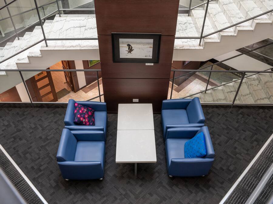 A modern lobby with a marble staircase, a framed artwork on the wall, and two blue sofas with a small table in the center.