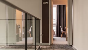 Pasillo de hotel con un separador de vidrio, una puerta con el número 309 y dos sillas en la habitación contigua.