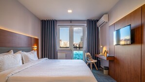 Habitación de hotel con una cama grande, un escritorio, una silla, un televisor y vistas a la ciudad desde la ventana.