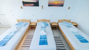 Una habitación con tres camas individuales, cada una con cabecero de madera y una toalla a rayas. En la pared, dos cuadros representan atardeceres.