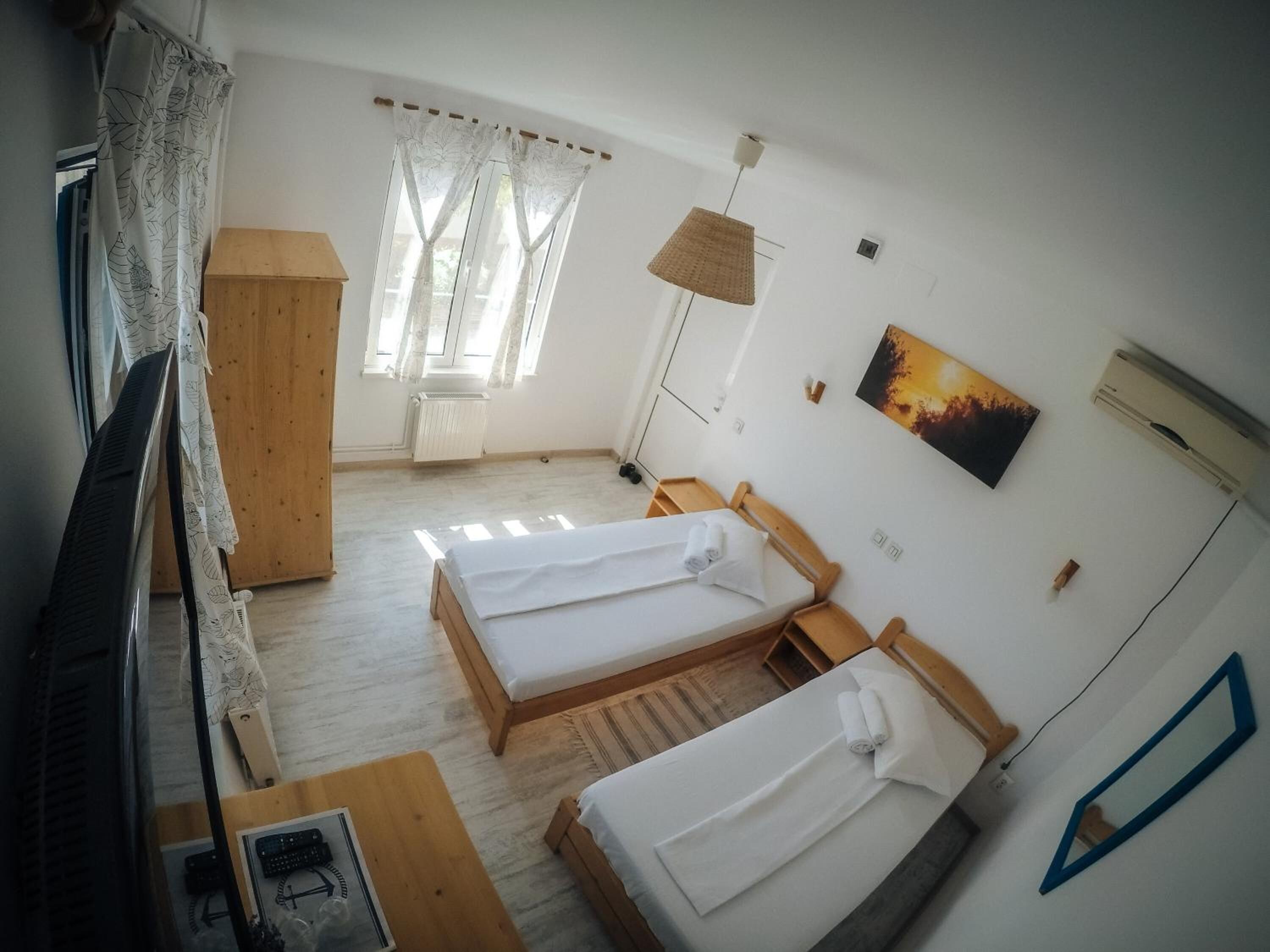 Habitación de hotel con dos camas individuales, un escritorio de madera, televisión, radiador y ventana con cortinas.