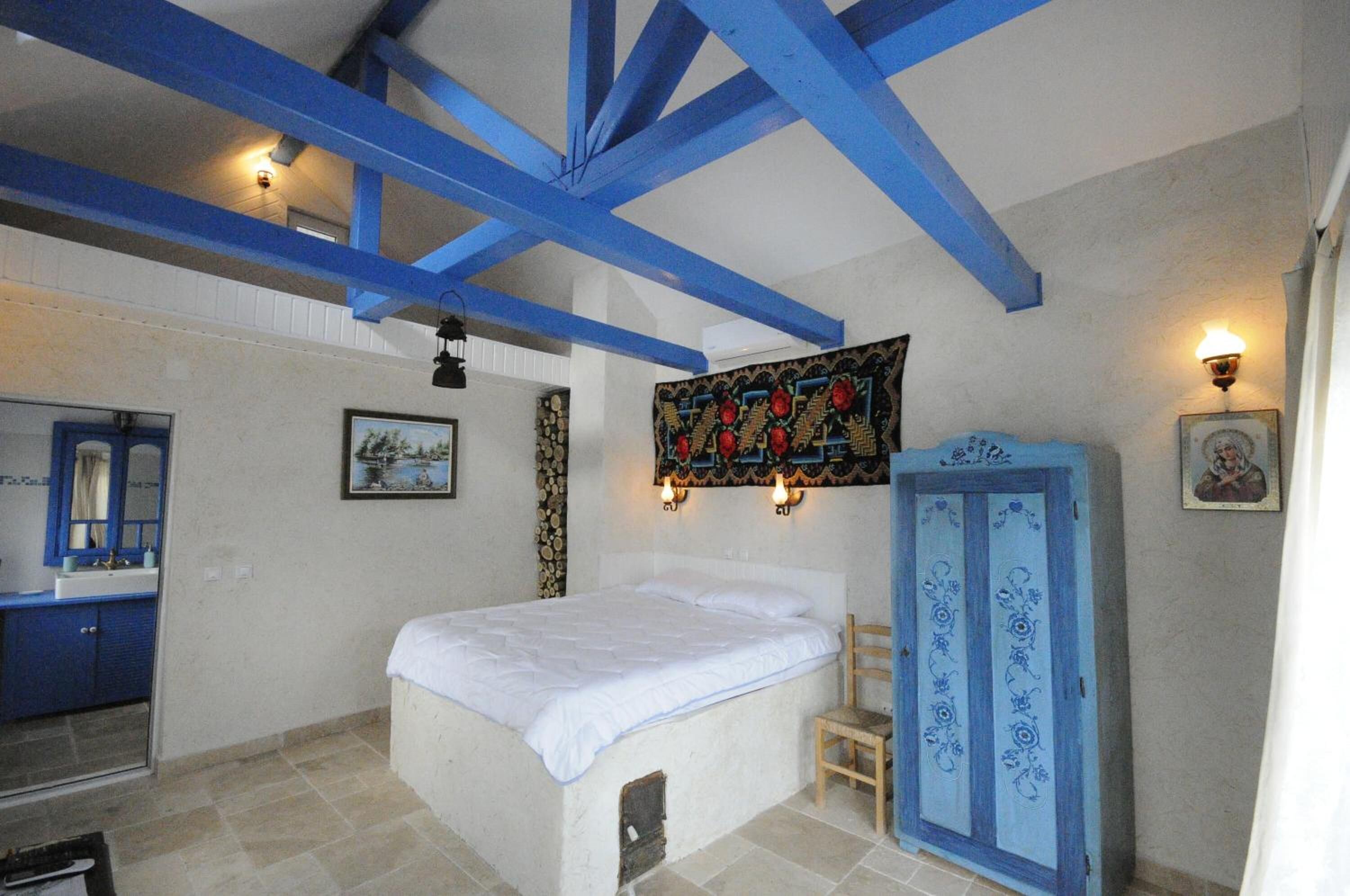 A bedroom with a bed, a blue wardrobe, a wall-mounted tapestry, and a bathroom with a blue cabinet.